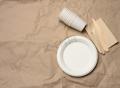 棕色纸背景上的一次性圆形白纸盘子和杯子