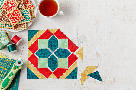 拼布块形状的布片、一堆模仿拼接块图案的饼干、一杯茶、缝纫和绗缝配件