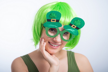 戴着绿色假发和滑稽眼镜的快乐年轻女性在白色背景下庆祝圣帕特里克节