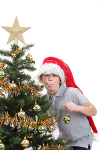 戴着圣诞帽的男孩在圣诞树上伸出舌头