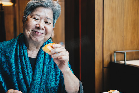年长的亚洲老年老年妇女在餐厅吃面包。