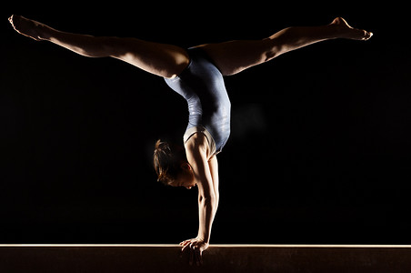 平衡木摄影照片_体操运动员在平衡木上做分裂倒立