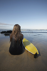 坐在沙滩冲浪板上的年轻女子的后视图