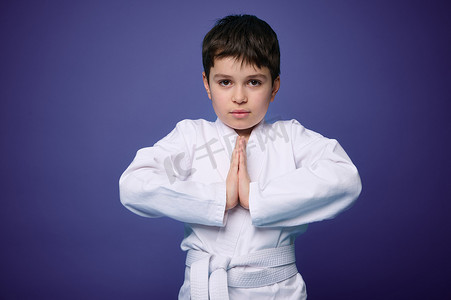 儿童跆拳道摄影照片_一个强壮的欧洲少年的腰长肖像，合气道战士在紫墙背景下练习武术，复制广告空间