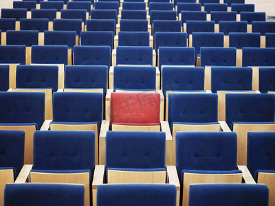 红色会议邀请函摄影照片_礼堂一大群蓝色座位中的一个红色座位