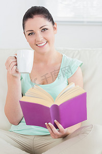 居家喝酒摄影照片_坐在沙发上边喝酒边看书的女人