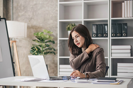 年轻的亚洲女商人在笔记本电脑上工作，压力很大，在办公室工作时头痛并努力思考。