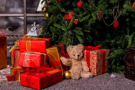圣诞树下的礼物，玩具熊和盒子，一个舒适的家庭新年的概念。熊等待圣诞老人，圣诞红色礼盒。泰迪熊和礼物放在圣诞树下。
