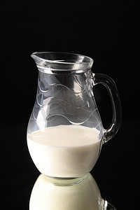 牛奶玻璃壶摄影照片_黑色背景中加牛奶的玻璃壶