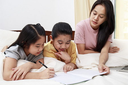 女儿们摄影照片_亚洲家庭母亲和她的女儿们在床上一起做家庭作业我