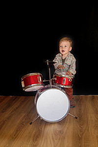 两岁的白人男孩正在演奏在黑色背景下被隔离的架子鼓