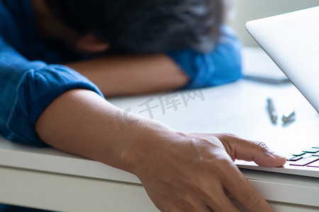 男人睡在桌子上，笔记本电脑放在桌子上，男人工作累了