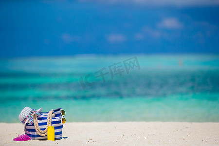热带海滩上的蓝色包、草帽、人字拖和防晒瓶