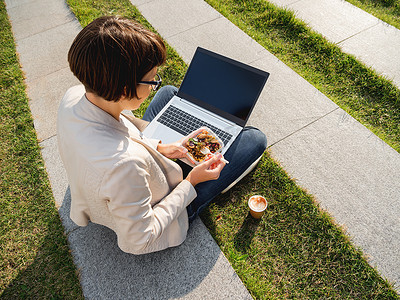 午餐盒摄影照片_“女人拿着笔记本电脑坐在公园长椅上，拿走了午餐盒，ca”