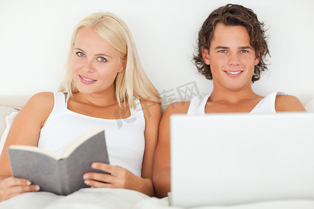 男人拿着笔记本电脑，而他的女朋友正在读书