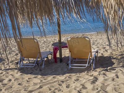 在希腊沙滩上用绿松石清澈的海水关闭两张带太阳伞的黄色空日光浴床