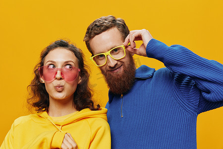 广告黄色摄影照片_一对男女欢快地微笑着，戴着眼镜，在黄色背景、符号标志和手势、家庭拍摄、新婚夫妇中歪着头。