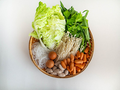 泰式寿喜烧汤配料包括蘑菇香肠猪肉丸牵牛花大白菜粉条芹菜鸡蛋在篮子上，白色背景