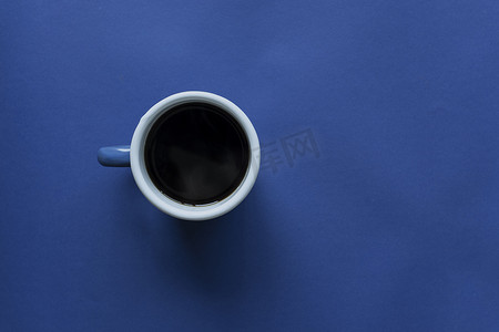 蓝纸背景中的一杯咖啡，深蓝色色调图像