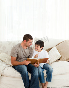 可爱的男孩和他父亲坐在沙发上看相册