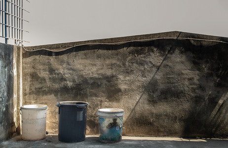 水泥桶摄影照片_阳台屋水泥地板上的蓝色、白色和黑色旧塑料桶。