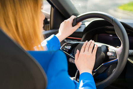按车喇叭摄影照片_身穿蓝色西装的女性驾驶汽车的后视图并按下汽车喇叭。