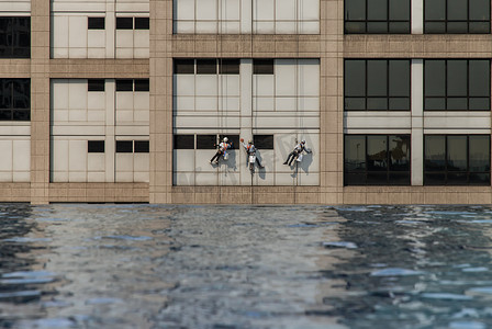 一组工人在高层办公楼清洁窗户服务，带反射 fiom 游泳池。