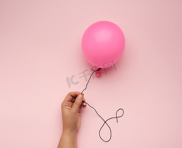 丝带气球摄影照片_粉红色背景上拿着充气粉红色气球的女手
