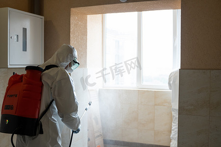 May摄影照片_UKRAINE, KYIV - May 20, 2020：身穿白色防护服和面具的男子正在对建筑物内表面进行消毒，同时冠状病毒流行以预防感染和控制流行病。