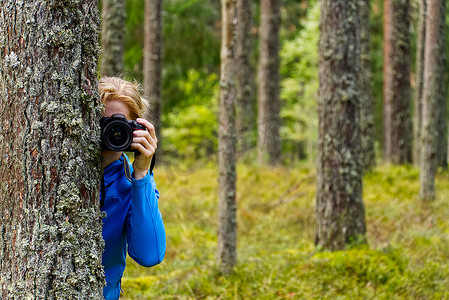 树林间摄影照片_年轻女子在树林间徒步旅行并用相机拍照。
