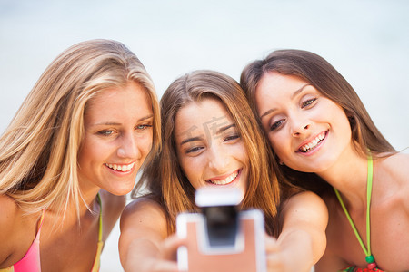 三个十几岁的美女在沙滩上用旧相机自拍