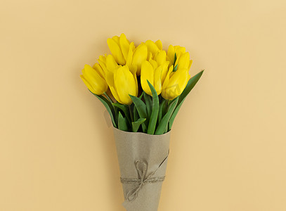 在米色背景上用牛皮纸包裹的黄色郁金香花束。