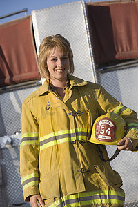 一位快乐的中年女消防员手持头盔的肖像，背景是消防队