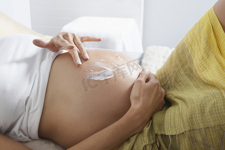 法国的卧室摄影照片_孕妇在床上腹部涂抹乳液的腹部