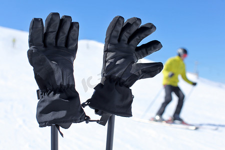 冬天阳光摄影照片_滑雪杆上黑色滑雪手套的细节，滑雪者模糊