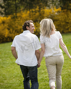 一对夫妇牵着手背对着镜头跑过公园