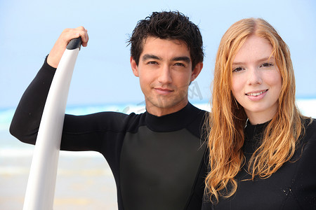好少年摄影照片_两个穿着潜水服的少年拿着冲浪板站着