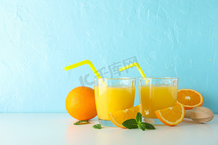平铺组合物，包括新鲜橙汁、木制榨汁机、薄荷、橙子和木制榨汁机，放在白色桌子上，背景为彩色，文字空间。