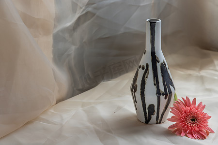 黑色和白色手工陶瓷花瓶，粉色花朵装饰在腮红纹理桌布上。