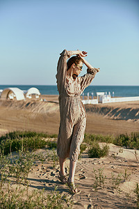 穿着米色连衣裙的时尚女性在大自然的大风天气中高高举起双臂