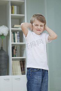 沮丧摄影照片_沮丧的男孩在家里用手捂住耳朵