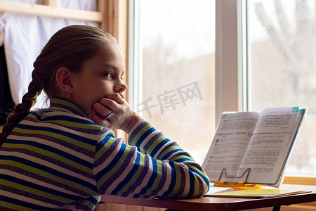 一个女学生坐在窗边的桌子旁做作业，女孩心烦意乱，看着框架