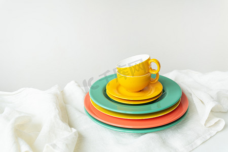 铺着亚麻桌布的白色桌子上放着空的黄色杯子和色彩鲜艳的盘子。