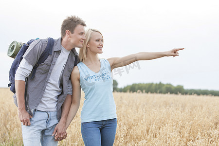 快乐的女徒步者在晴朗的天空下向田野上的男人展示一些东西