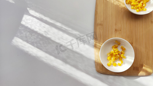 盘子里有很多黄色玉米罐头，盘子在白色背景的木竹砧板上。