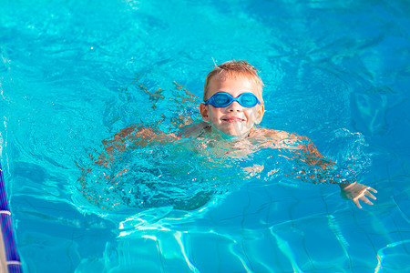 快乐的太阳摄影照片_戴着护目镜在游泳池里游泳的可爱快乐小男孩