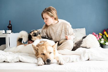 快乐的年轻女人坐在床上和她的狗玩耍
