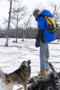 宠物狗玩耍摄影照片_男人在森林里和狗玩耍，在地上玩雪