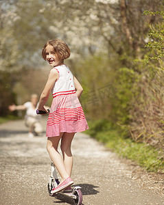 在公园里骑滑板车的小女孩远离相机到妈妈身边