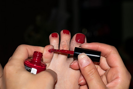 女孩脚趾摄影照片_晚上在家女孩的手在脚趾上涂红色指甲油